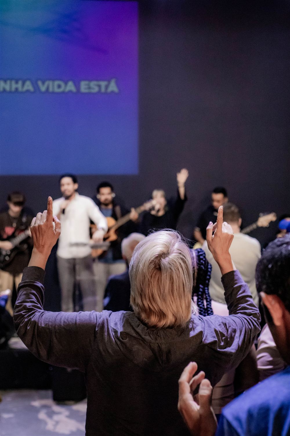 Mulher de costas com as mãos erguidas em adoração, diante da banda
