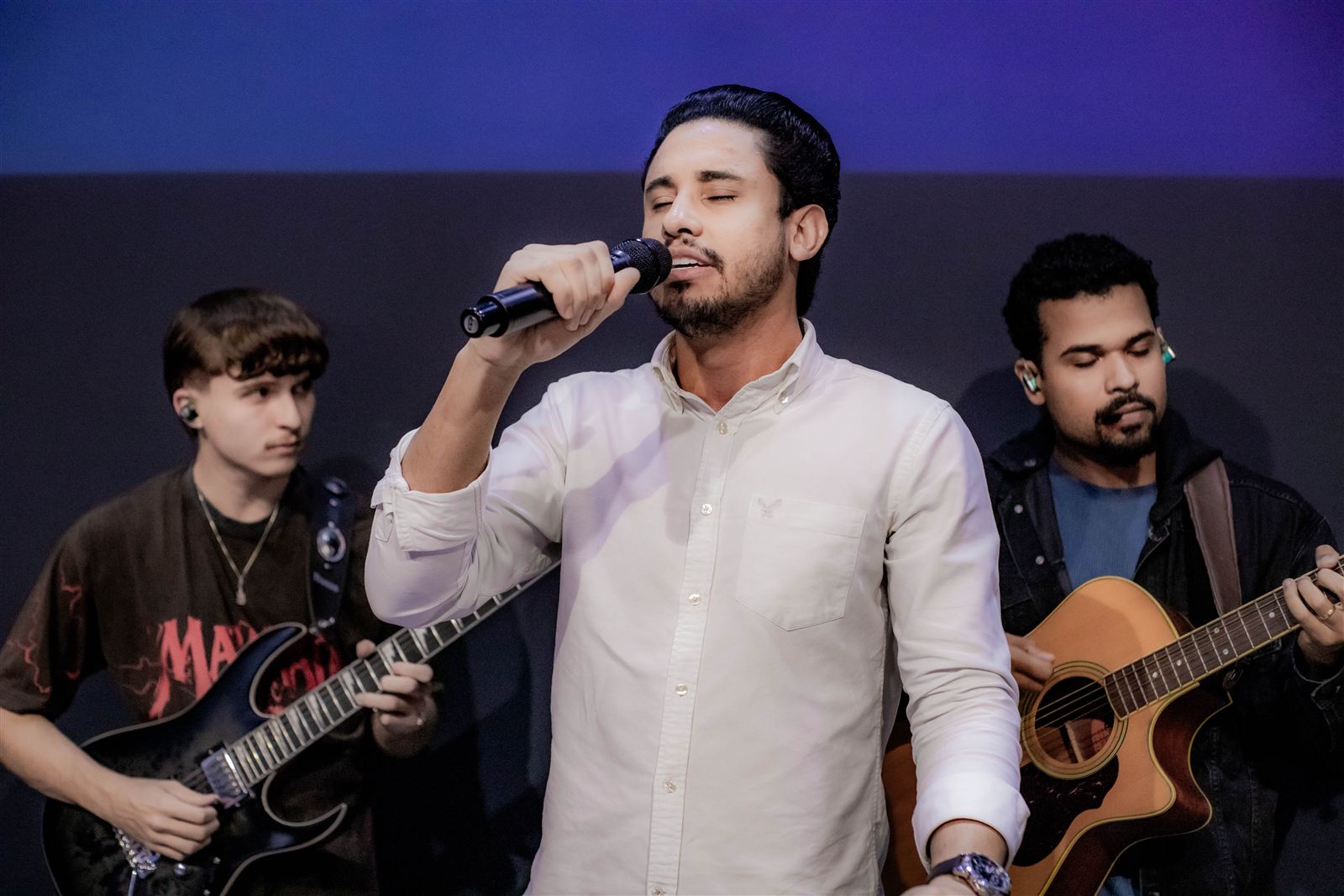 Pastor Kaic cantando ao microfone, acompanhado pelos músicos