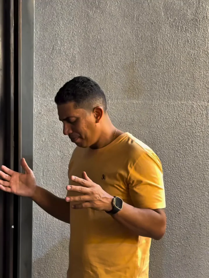 Homem de camiseta amarela orando com as mãos abertas
